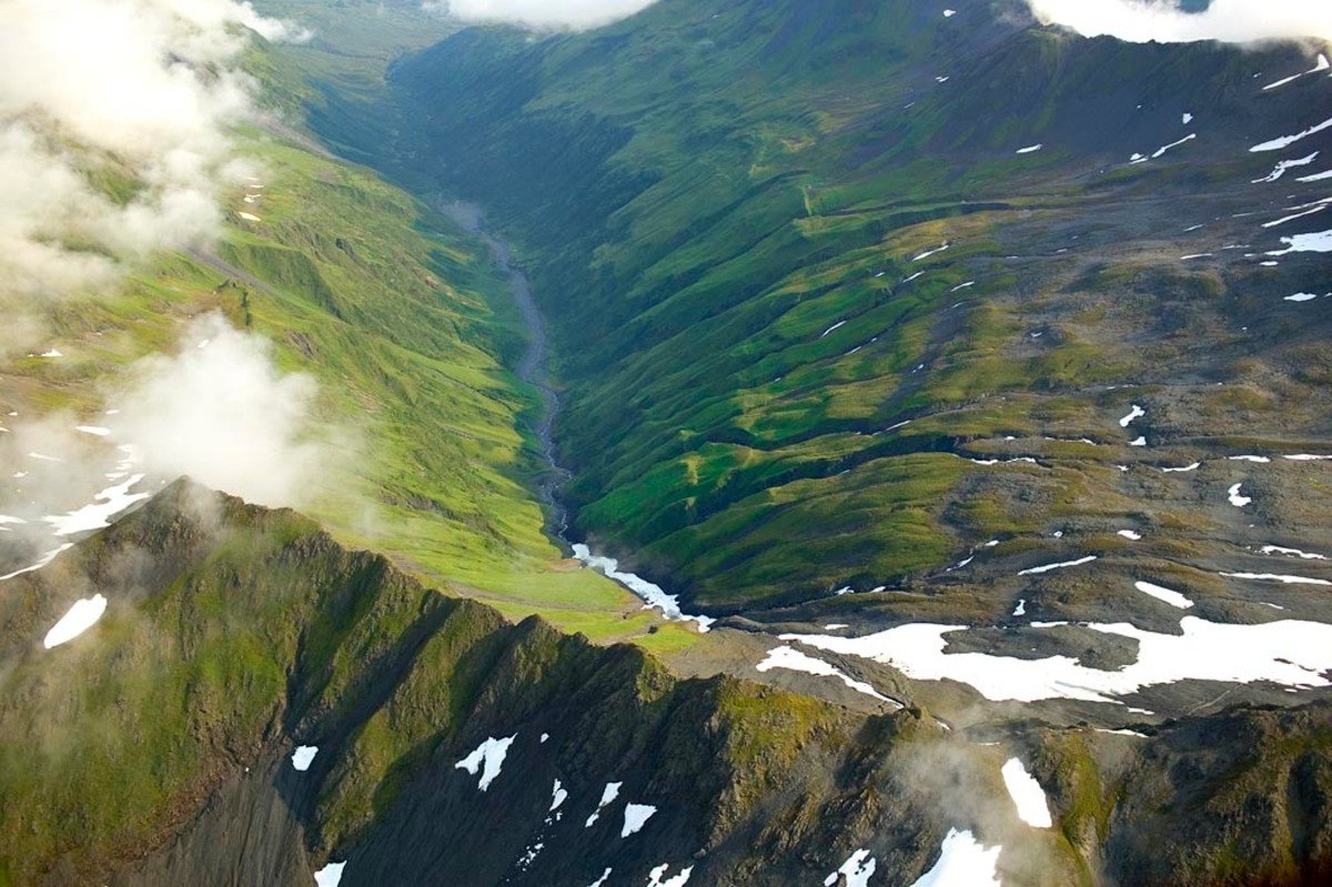 Aerial view of green mountain ridges, a river drainage and patches of snow at Kodiak National Wildlife Refuge, Alaska