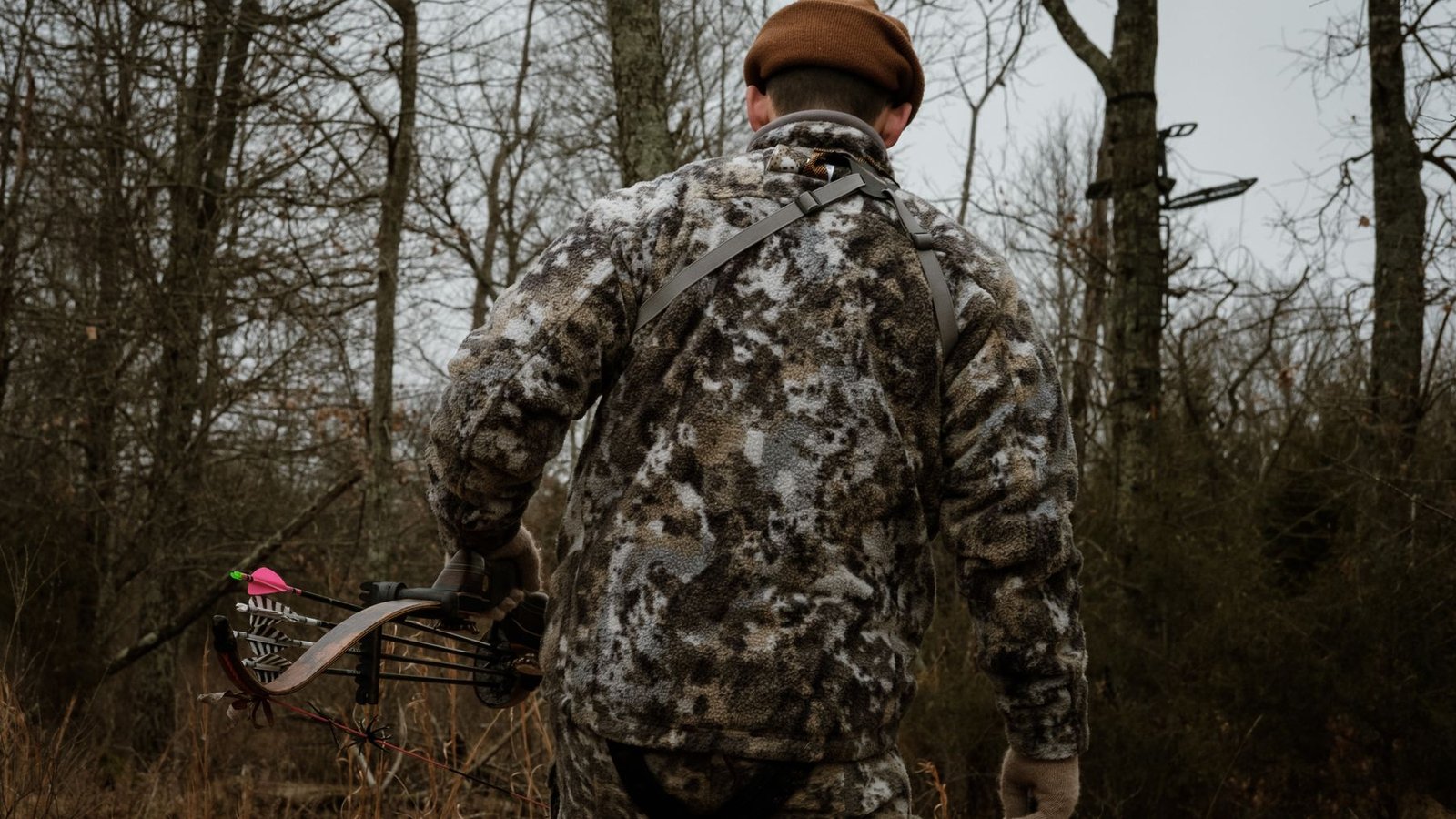 Bowhunter in camouflage walking through a winter forest.