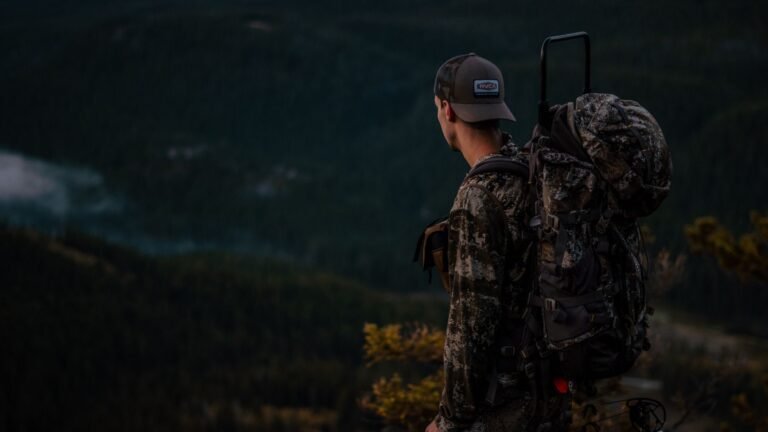 Bowhunter in camouflage carrying a loaded hunting pack in mountain country